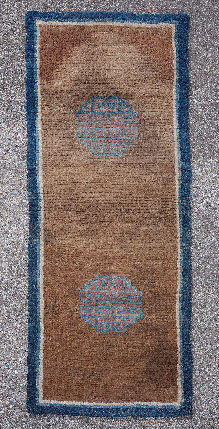 This stunning Tibetan monastic rug is a rare collectors’ piece. 

The simplicity and balanced use of space have resulted in a pleasing piece of Tibetan woven art. Two simple geometric medallions float on the brown central field, surrounded by