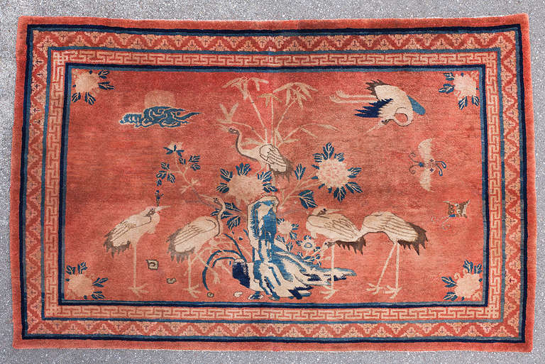 A warm red tone dominates this charming Inner Mongolian pictorial rug. 

Chinese pictorial rugs exude a certain charm and often appear like a framed window, offering a glance into a different world. The scene is set by a central rock with bamboo,