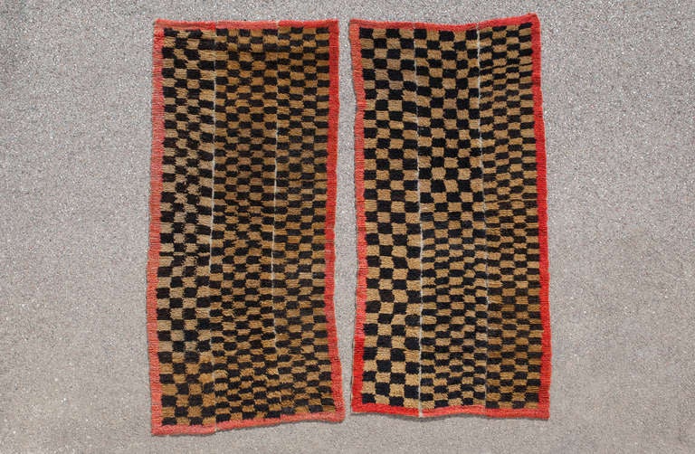 This is a rare and highly collectable pair of Tibetan Tsutruk rugs. Checkerboard rugs are hard to find and even more rare as a pair. The checkerboard pattern consists of irregular squares in brown and ochre and is framed with a simple red border.