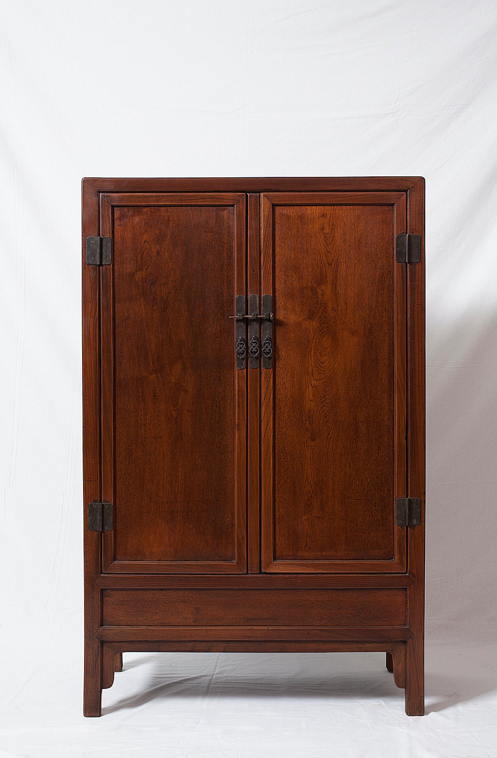 The master carpenters of Suzhou in Jiangsu province made this Minimalist, perfectly proportioned square-corner cabinet. 

Made from honey-colored elmwood, this cabinet has two doors with a removable stile in between and a panel below the doors. A