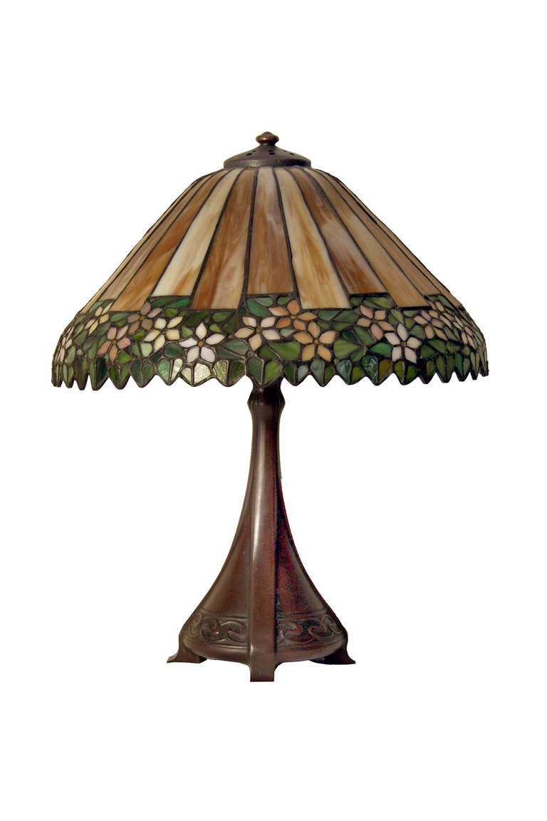 Table lamp with three socket base with a floral leaded glass shade. The lamp measures 21 inches in height and the shade is 18 inches in diameter.
