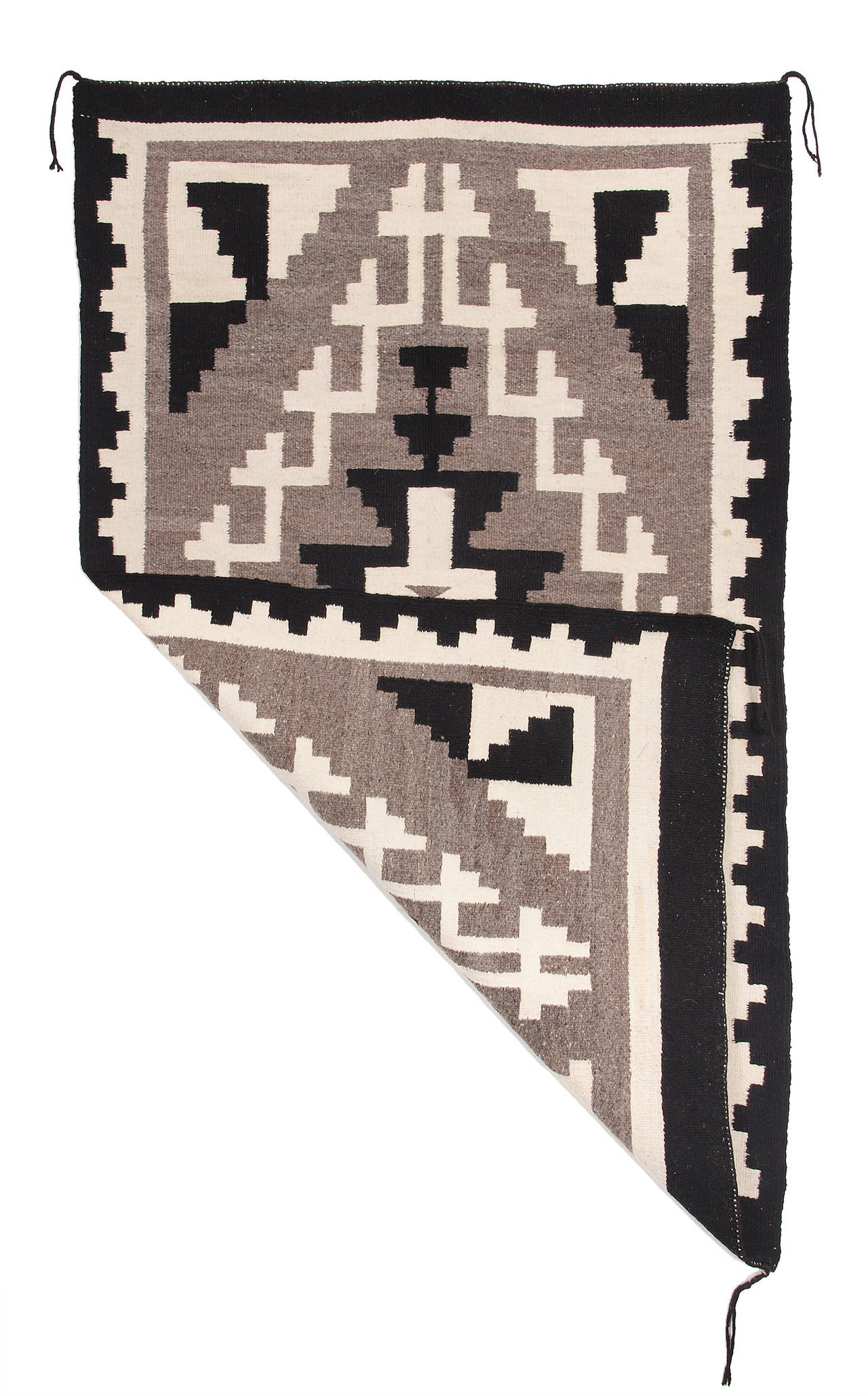 A pan-reservation or trading post rug woven by a Navajo artist circa 1950 in natural ivory, gray and black fleece. A traditional geometric and hooked design with a beautiful variegation in the gray background.

This textile is well suited for use
