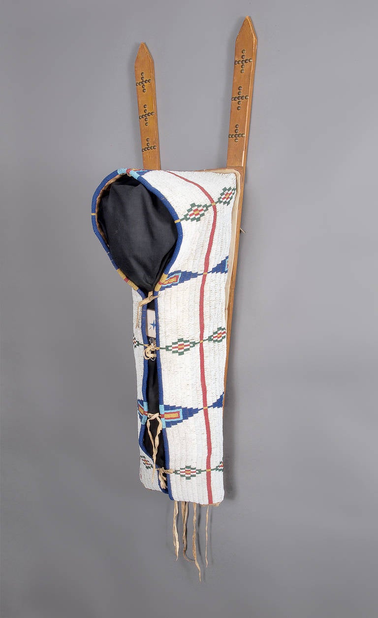 A late Classic period fully beaded cradle (papoose). Constructed of native tanned buffalo hide, sinew sewn with glass trade beads, trade cloth and wood. Beaded in Classic Cheyenne motifs including stylized tepees, tipis with a red 