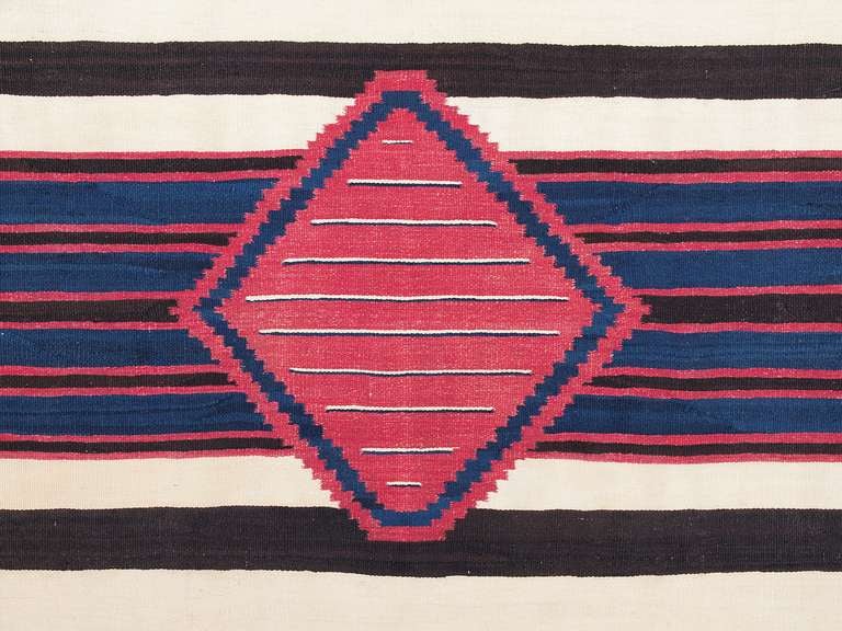 This is an exceptional classic period (pre-reservation) Navajo chiefs wearing blanket. It is very finely woven of native handspun wool in natural brown and ivory fleece; the blue is indigo dye and the red is cochineal dye.  The nine-point diamond