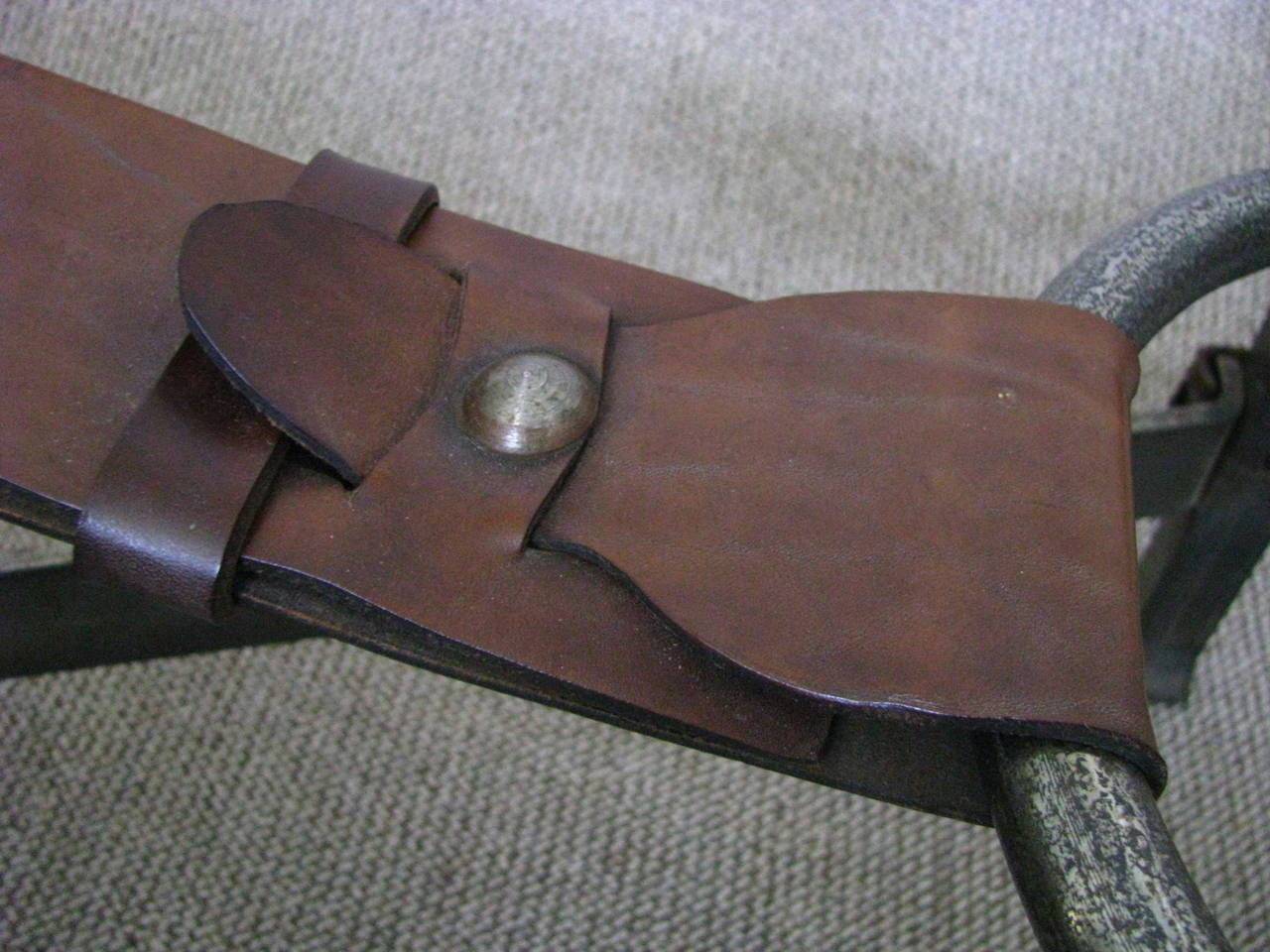 Style of Jacques Adnet, forged from cast iron riveted with corner brackets and thick saddle stitched brown leather straps harnessed to the four corner hitching posts from a center iron ring. Patination of iron frame shows a silver tone with charcoal