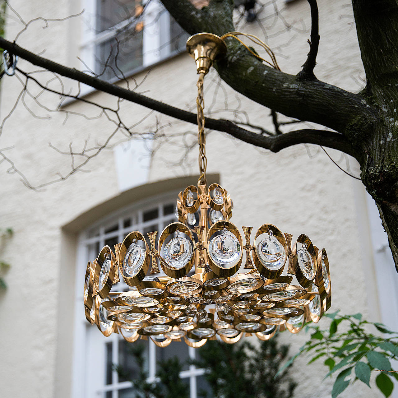 Elegant round chandelier made of textured gilt brass with concave and convex teardrop beveled crystal prisms within the outer rings of the chandelier structure. Five brass stick lights.