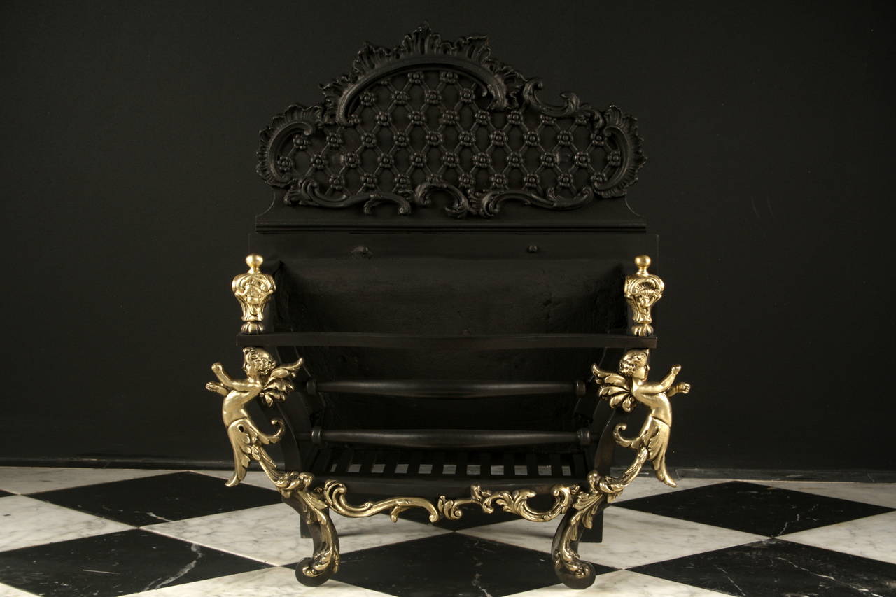 An original & attractive Rococo revival brass and iron Fire Basket, with elaborately cast brass fret, legs with winged cherubs and finials, with cartouche shaped back plate, English late 19th century.

Depth: 11