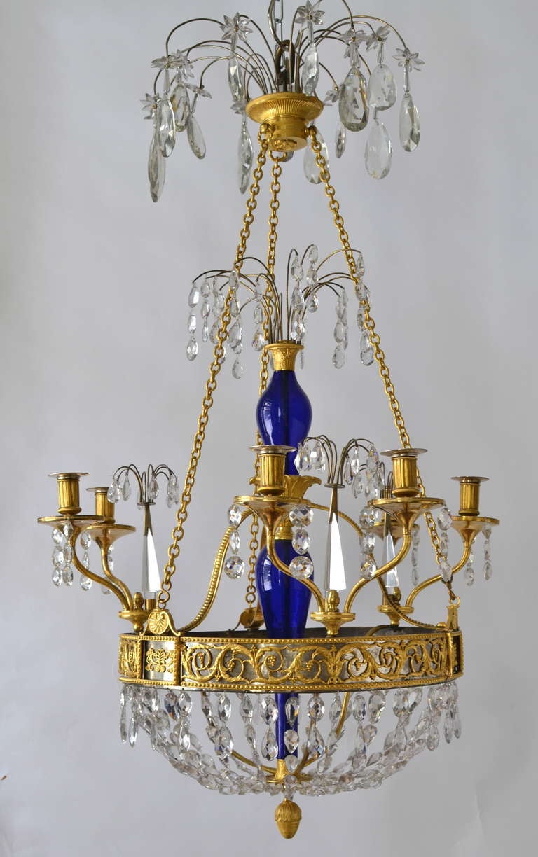 A Russian chandelier, first half of the 19th century.  Gilt bronze with a blue glass center stem. Unusual ring holding the gilt bronze candle arms with it´s decorations of gilt bronze on top of a polished steel bottom.