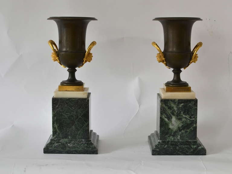 A fine pair of medici shaped patinated bronze urns with gilt bronze mounts on green and white marble bases. Possibly Italian and made circa 1820.