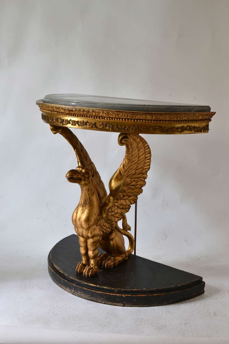 A Swedish empire demi lune console table with a grey marble top. Carved giltwood, part of the decoration is gilt lead. Made in Stockholm or Gothenburg circa 1820. Unusual model.