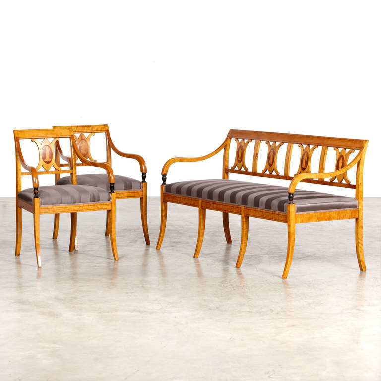 Elegant Swedish Empire set consisting of a pair of armchairs and a bench, done in birch with inlays, Sweden, circa 1810. 
The backs with inlays in the form of Greek female figures. Beautifully executed. The set is reupholstered with Villa Nova.