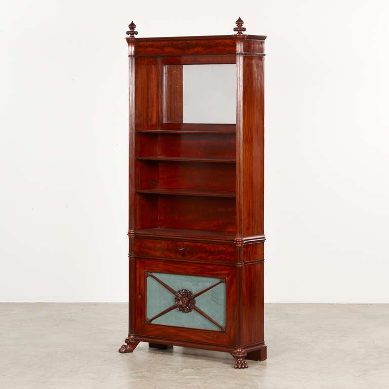 Bookcase crafted in Cuban Mahogany with grooved quarter pillars. Carved top corners. Top with mirror and shelves. Lower part with door with jadegreen velour and cross bond in mahogany.  A furniture crafted with high craftsmanship.  Gustav Friedrich