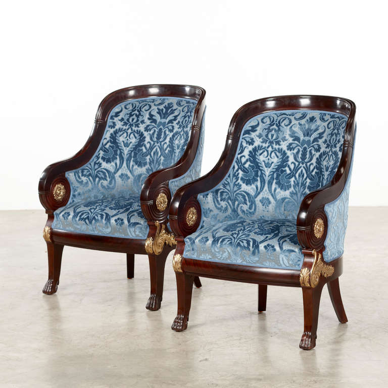 Pair of Bergeres in Russian Empire Style crafted in massive Cuban Mahogany with giltwood carvings of rosettes and leaves. The legs ends up in animal paw feet. Crafted with high craftsmanship. 
Newly upholstered with fabric from Levievre. 
Denmark,
