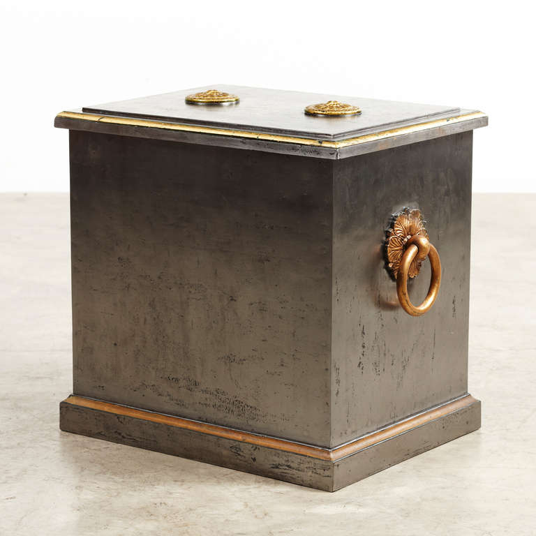 Large safe in polished iron. Top with giltwood rosettes hiding the keyhole and  sides with giltwood handles. Below the lid, key locker with eight pawls, two in each side. The simplicity and finish of the iron safe gives it a smart and modern