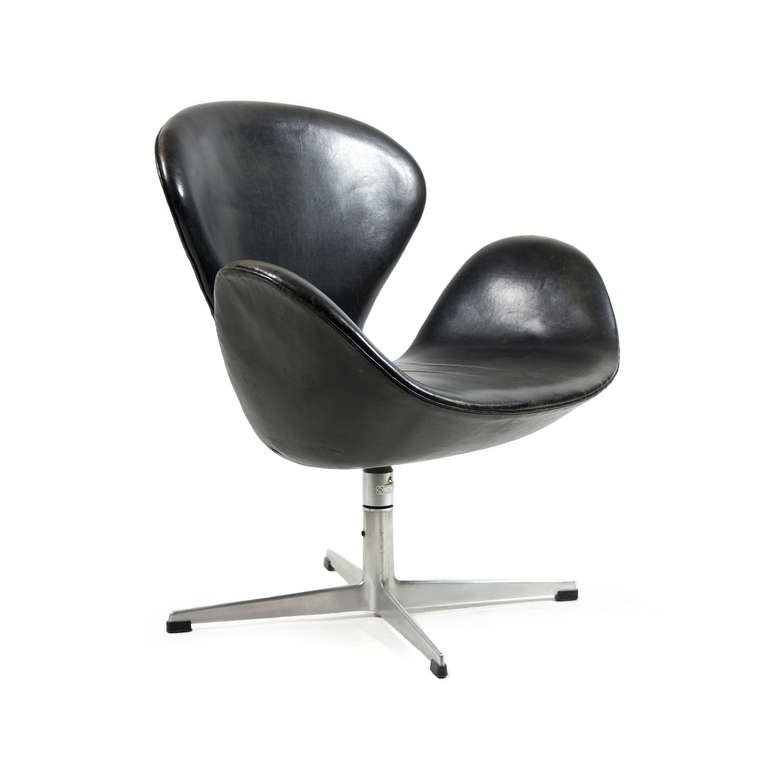 A swan chair designed by Arne Jacobsen upholstered with original black-dyed natural leather.  
This model has tilt-function which is rarely seen in these first editions.  Rich patinated black-brown leather in fine condition.  

Manufactured by