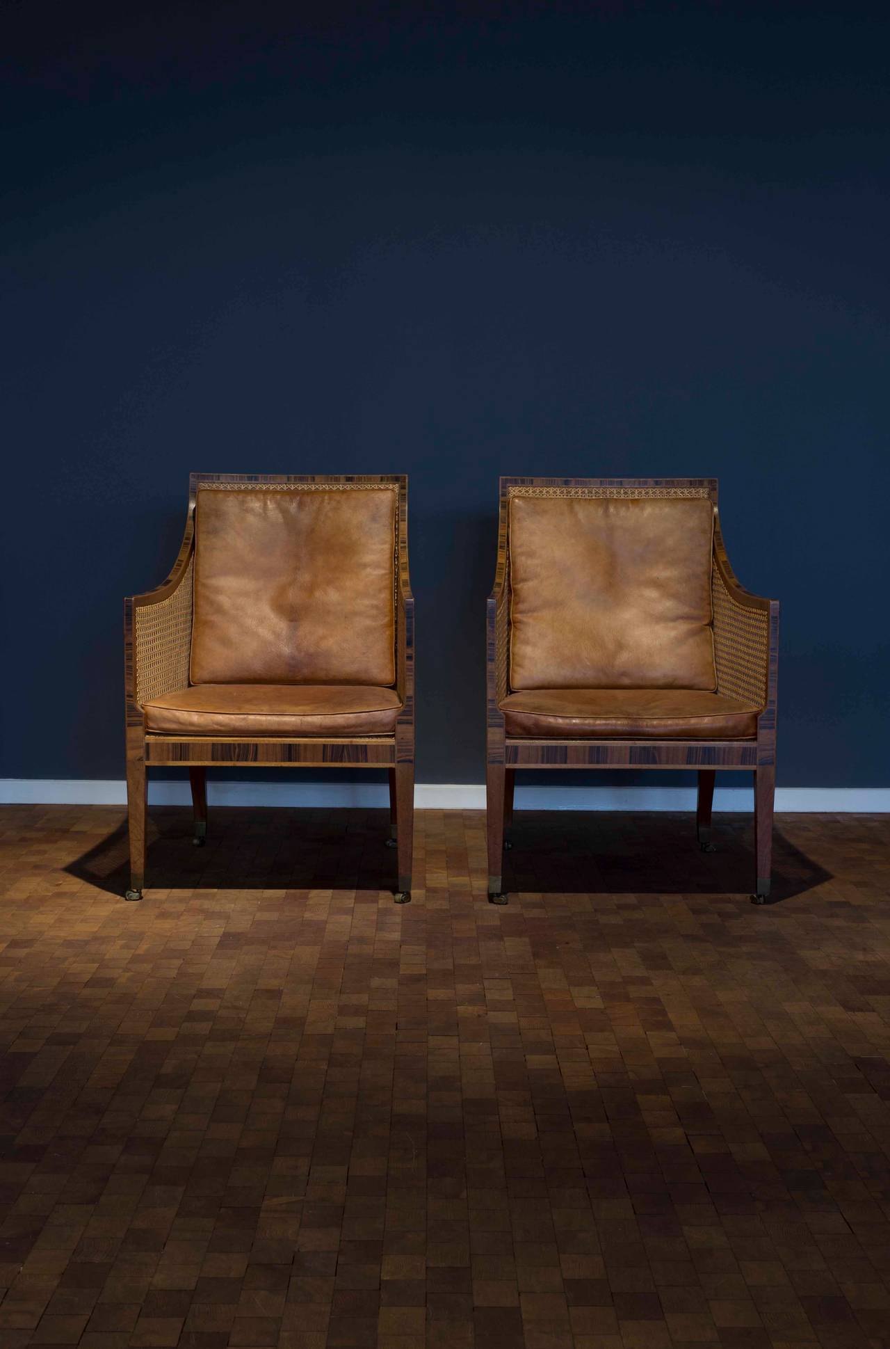 A pair of early and rare Kaare Klint 'Bergere' or 'English chairs.' 

Frame of mahogany with rosewood inlays, woven French-style cane and brass casters. Original loose cushions upholstered with Niger leather. 

Designed by Kaare Klint, 1932,