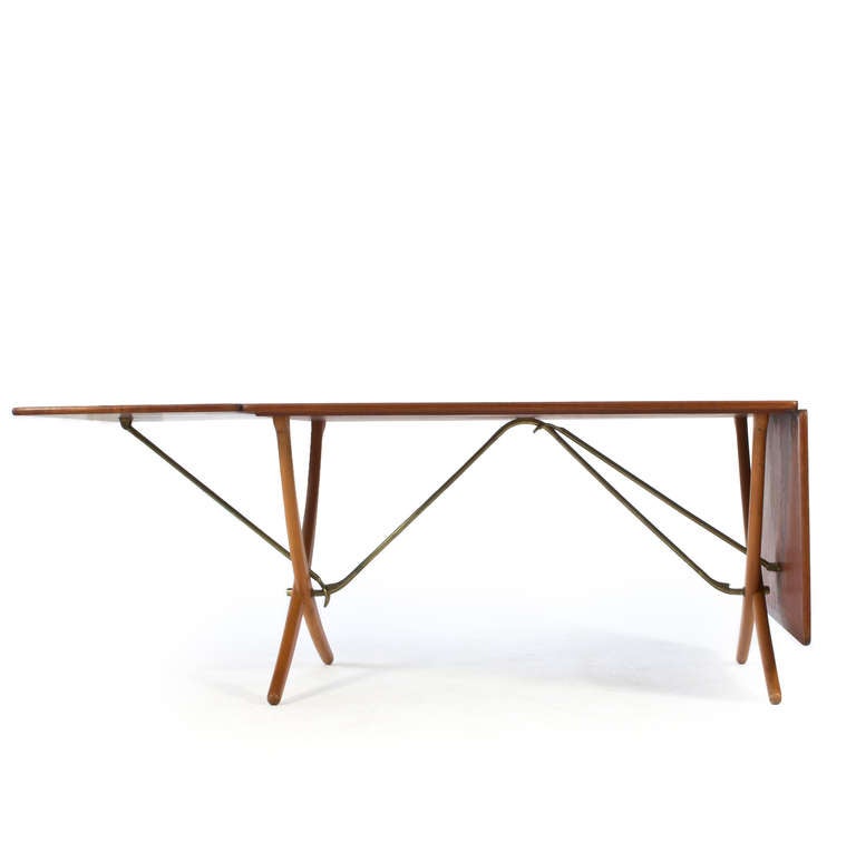 Hans J. Wegner teak dining table with two drop-leaves, cross-legs of patinated beech and stretchers of brass. 

Manufactured by cabinetmaker Andreas Tuck, Denmark, model AT304. 

Measuring 128 cm/ 50 Inches or 238 cm / 94 Inches when fully