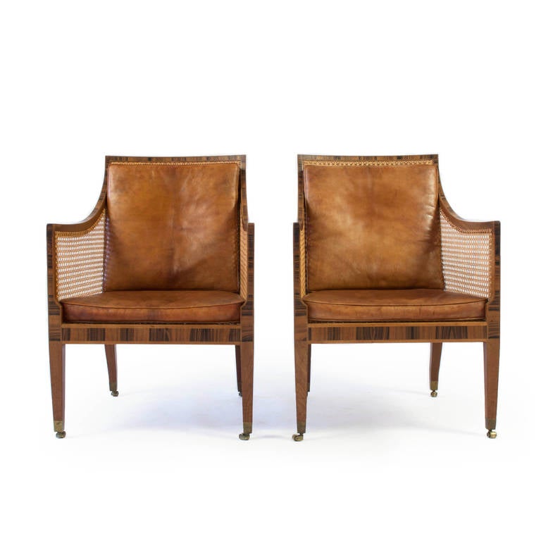A pair of early Kaare Klint 'Bergere' or 'English chairs'. 

Frame of mahogany with rosewood inlays, woven French-style cane and brass casters. 

Original loose cushions upholstered with Niger leather. 

Designed by Kaare Klint 1932,