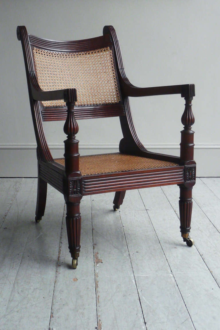 An interesting and particularly fine quality early Anglo Indian padouk bergere, the caned seat and back within a scrolling and reeded frame, terminated by carved rosettes and patterae, the arms on vase supports and turned reeded legs, raised on good