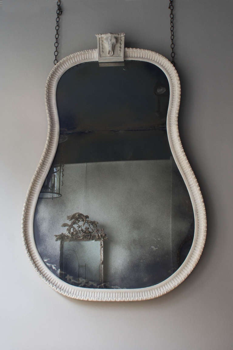 The traditionally constructed and confidently carved pine and limewood frame is surmounted with a Bucranium or Ox's skull, finished in a textured gesso, and contains a cleverly distressed mirror plate in two parts

In the English Classical late