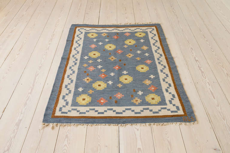 Beautiful Swedish woven flatweave wool rug by Anna-Greta Sjöqvist. Blue background with ivory border and pattern in yellow, pink, coral and brown shades. Mid-century.