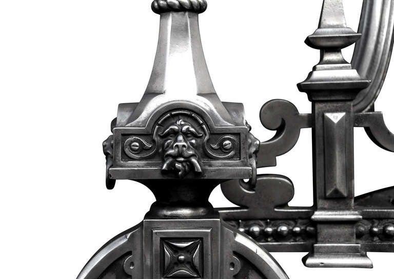 A very large English firegrate in the Jacobean Baroque style. The protruding cast iron firedogs with horseshoe bases surmounted by gargoyle mask, gadrooned motif and globe finials in the Celtic manner. The beaded fret and heavy top bar flanked by