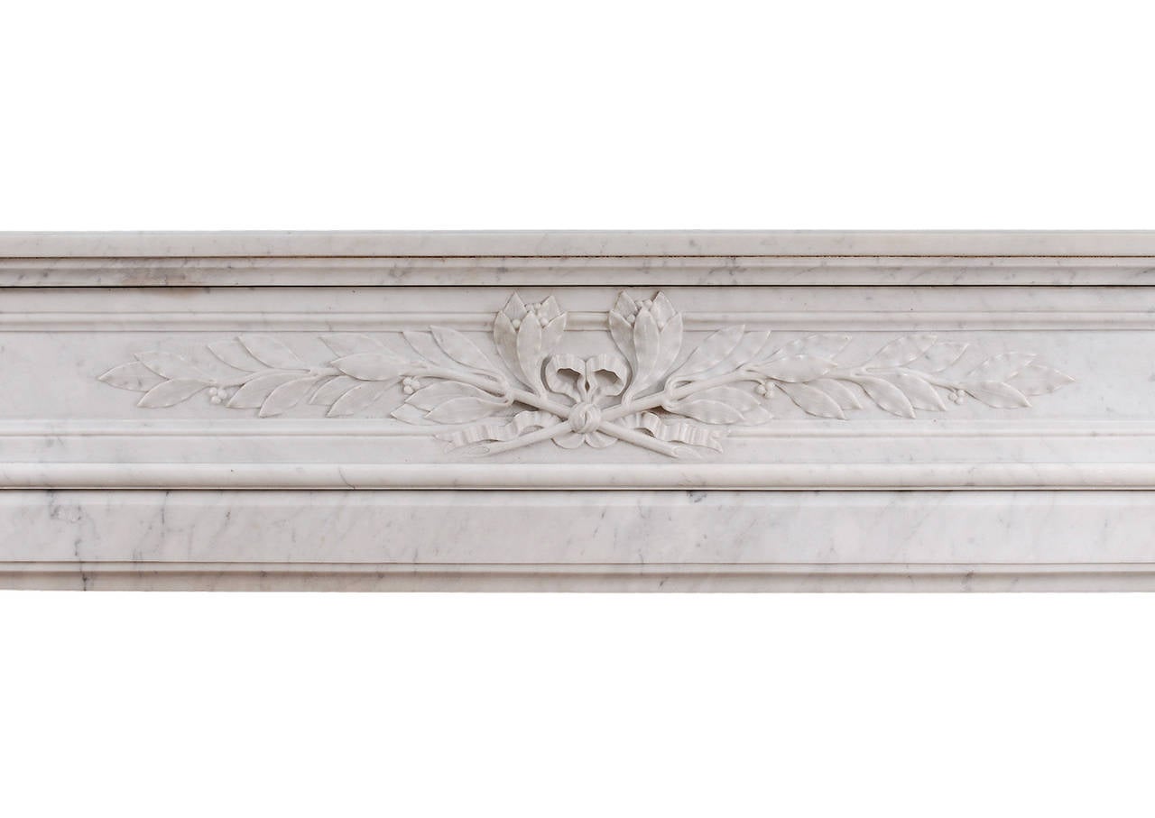 A 19th century French Louis XVI style fireplace in light Carrara marble. The carved, panelled frieze with tied laurel leaf and foliage to centre. The jambs with tapered, fluted columns surmounted by carved capitals. Panelled outgrounds. Shaped
