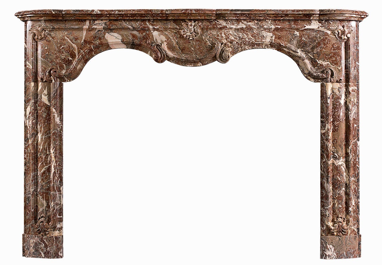 A period 18th century Louis XIV/XV transitional fireplace in Languedoc marble. The shaped, panelled frieze with carved foliage and rosette to centre, the panelled jambs with matching carving to base. Shaped, moulded shelf. An elegant piece, circa