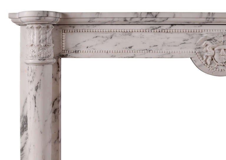A good quality French Louis XVI style fireplace in veined Statuary marble. The jambs with half rounded column, surmounted by carved acanthus leaf capitals. The frieze with beaded panels and carved female mask to centre. Shaped, moulded shelf. 19th