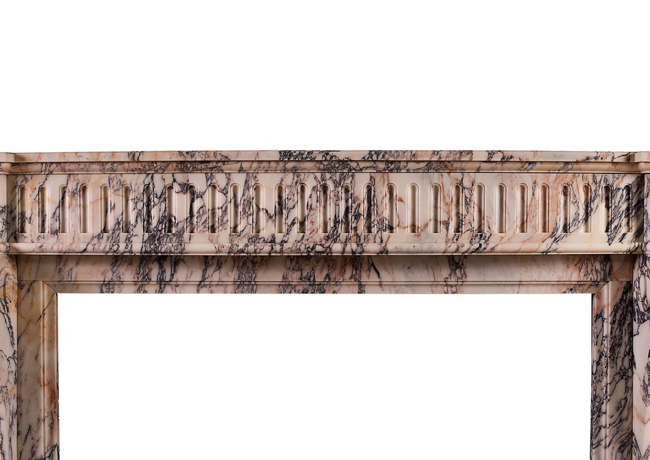 Ein französischer Marmorkamin im Stil Louis XVI aus dem 19. Jahrhundert. Die geformten, geschwungenen Pfosten mit geschnitzten quadratischen Patera darüber. Der gewölbte Fries mit durchgehenden Kanneluren und einem geformten, profilierten Regal