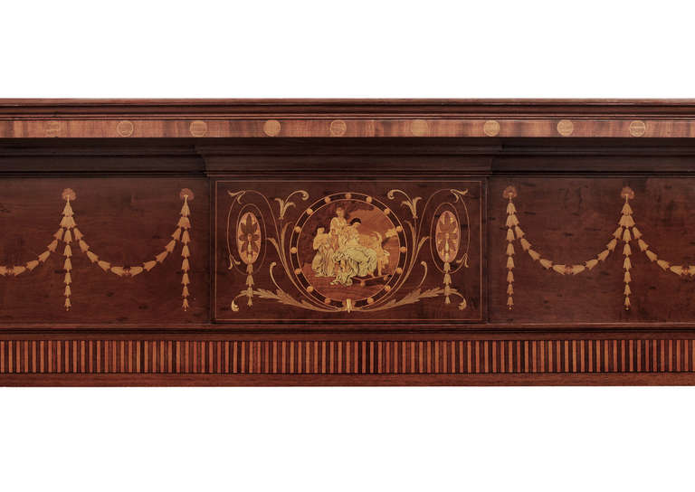 A 19th century English mahogany fireplace. The frieze inlaid with swags and bell drops, the centre panel with plaque featuring figures and foliage. The jambs with inlaid double panels and delicate bell drops, surmounted by bust and laurel wreath.