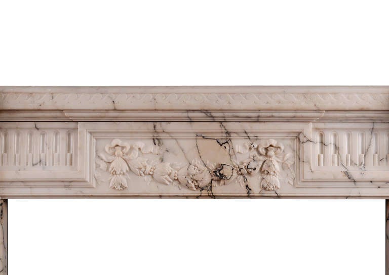 Une petite cheminée française de style Louis XVI en marbre Pavonazza clair. Les montants à panneaux sont ornés de clochettes finement sculptées de feuillages entrelacés, et surmontés de supports à écailles. La frise cannelée avec un bloc central