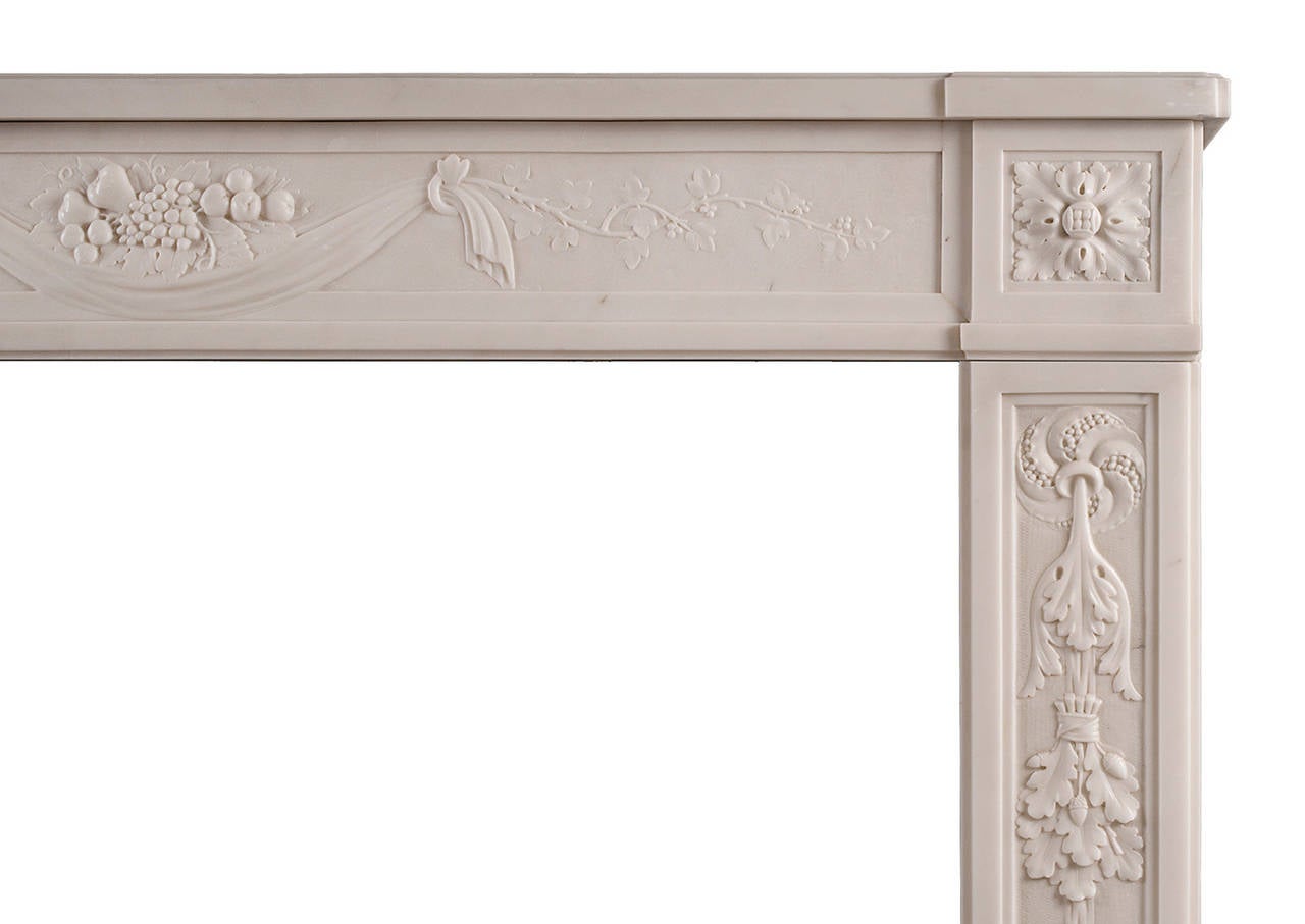 An 18th century French Louis XVI statuary marble fireplace. The carved frieze with arrangement of fruit and drapery to centre, flanked by finely carved foliage. The jambs with tied foliage and berries, surmounted by carved square paterae. Moulded