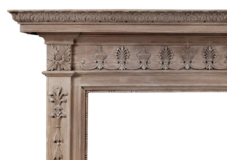 A carved English pine fireplace. The frieze with carved urns and honeysuckle, the jambs with carved bell drops and foliage surmounted by square paterae. The shelf with carved acanthus leaf moulding throughout. 20th century.

Shelf Width - 1562 mm 