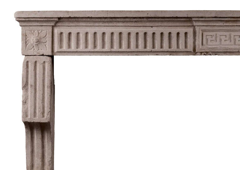 Un affascinante caminetto in pietra del XVIII secolo Louis Stone. Il fregio scanalato con pannello centrale a chiave greca, sotto la mensola modellata. Gli stipiti a forma di staffa con scanalature di arresto e patere quadrate intagliate sui blocchi