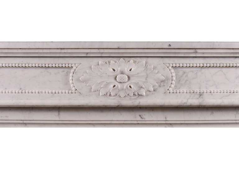 A good quality French Louis XVI style fireplace in Carrara marble. The frieze with carved oval paterae to centre and beading throughout. The jambs with carved acanthus leaves and beading to plinth. Shaped, moulded shelf. Attractive original brass