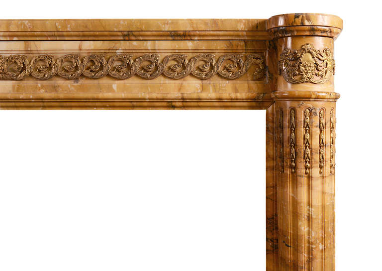 An impressive 19th century French fireplace with elaborate brass ormolu enrichments to frieze and jambs. The fluted half round columns inlaid with ormolu bellflower husks, surmounted by crest and figures. Guilloche foliage ormolu to frieze. Complete