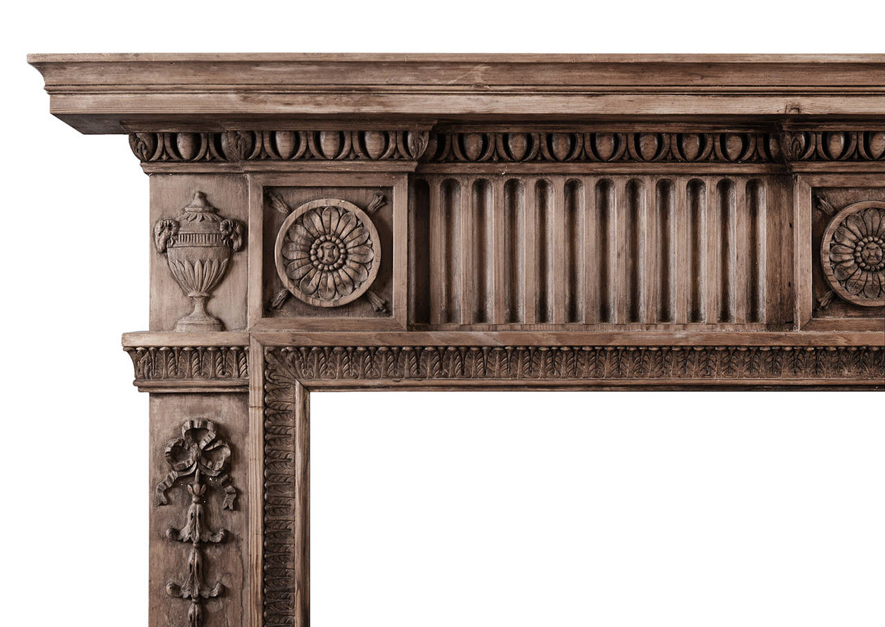 A carved pine fireplace with a late Georgian influence. Three carved flower paterae to frieze, rams head urn side blockings, and tied ribbon bellflower drops to jambs. Carved leaf inner moulding, and egg and tongue carving to moulded shelf, early