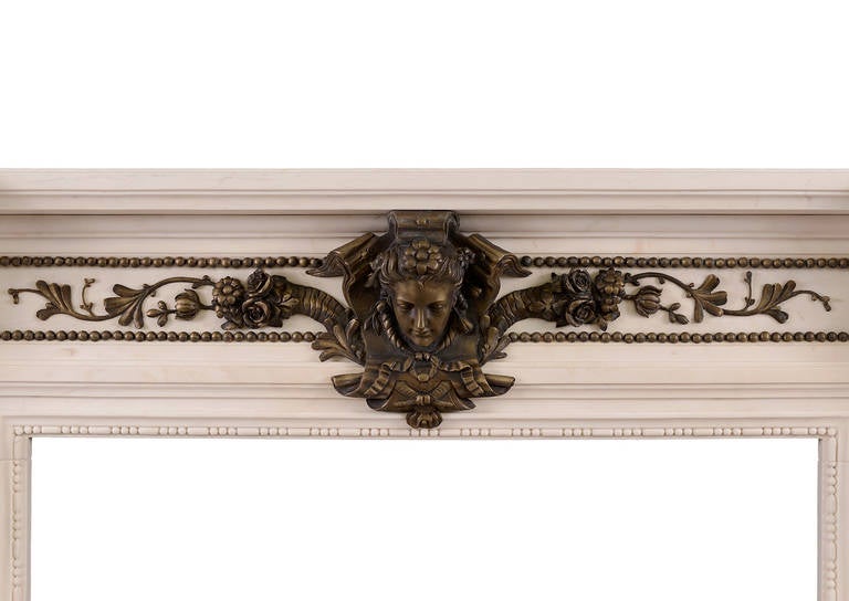 A striking Regency style fireplace in white marble with fine quality bronze detailing. The frieze with bronze female mask and ribbons with trailing foliage. The fluted jambs with carved inner mouldings, adorned with bronze female figures and stiff