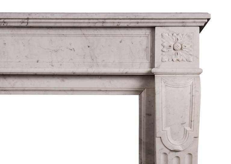 A 19th century French Carrara antique marble fireplace in the Louis XVI style. The panelled, stop fluted jambs surmounted by carved square paterae to end blockings. The panelled frieze with carved rosette patera to centre. Moulded shelf.

Shelf
