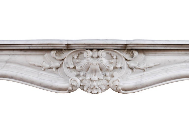 A 19th century French Louis XV style fireplace in Carrara marble. The panelled jambs with stiff acanthus leaves to base, sumounted by carved shell and scroll work. The panelled outgrounds with original brass vents. The panelled frieze with carved