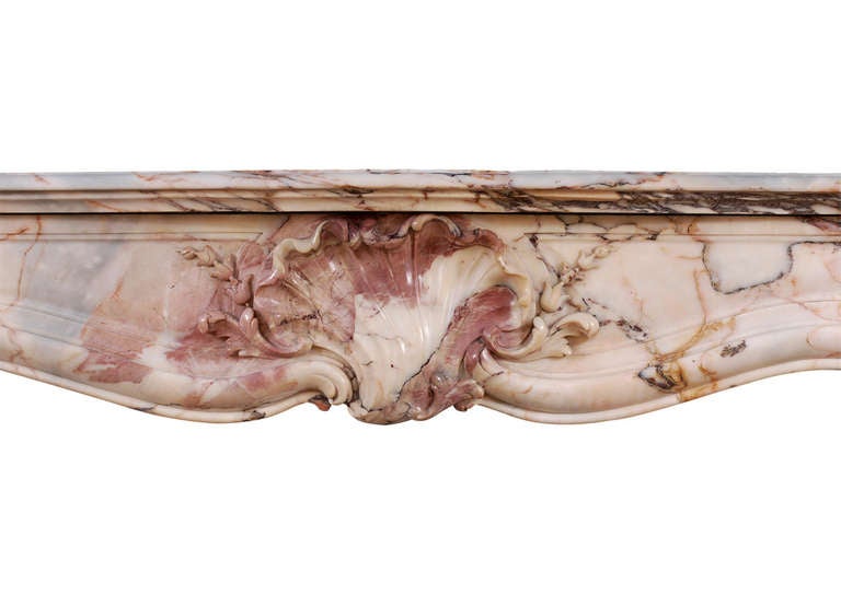 A fine quality 19th century French Louis XV style fireplace in Kuros Dore marble. The panelled frieze carved with intricate shell and foliage to centre, the shaped, panelled jambs with stop flutes surmounted by carved shell and scrolls. Shaped