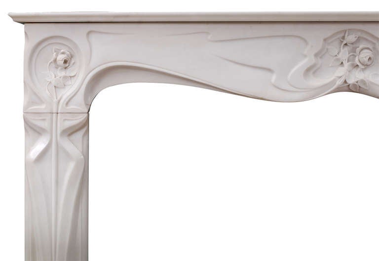 A refined French Art Nouveau white Statuary marble fireplace. The shaped frieze with delicately carved rose and foliage to centre and ends, the jambs with full length tapered panels. Moulded shelf. Late 19th-early 20th century. Very good quality