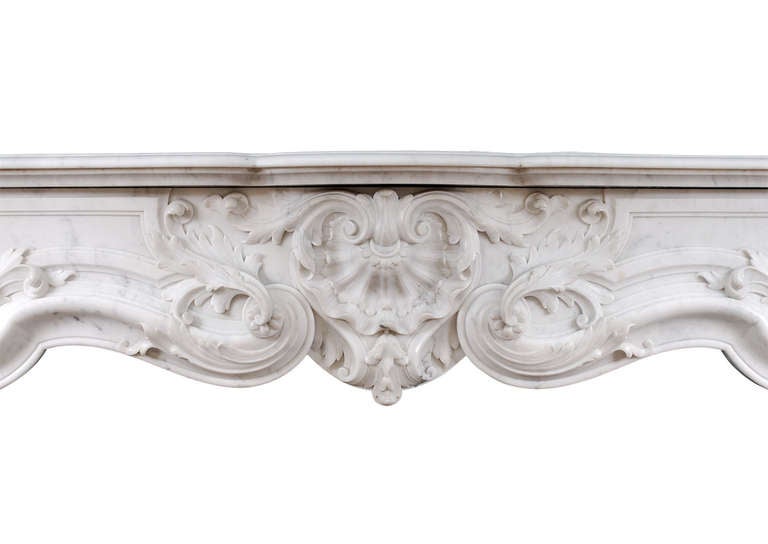 A very fine quality French Louis XV style marble fireplace in light Carrara. The panelled frieze with carved shell to centre flanked by foliage and belldrop below. The shaped jambs with stiff acanthus leaf to base surmounted by cartoosh with shell