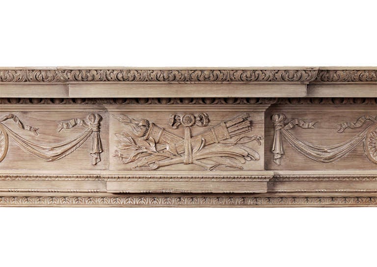 A large English wood fireplace in the Georgian style. The carved frieze with drapery and pateras, with centre blocking featuring quiver and foliage. The panelled jambs with carved bellflowers, surmounted by urn end blocking. Carved inner leg