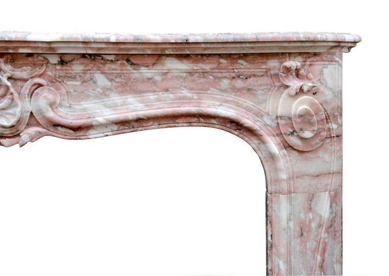 A French Louis XV style fireplace in Norwegian rose pink marble. The jambs with shaped panels surmounted by carved scrolls and foliage, the frieze with deeply carved shell to centre. Shaped shelf, late 19th-early 20th century.

Measurements:
Shelf