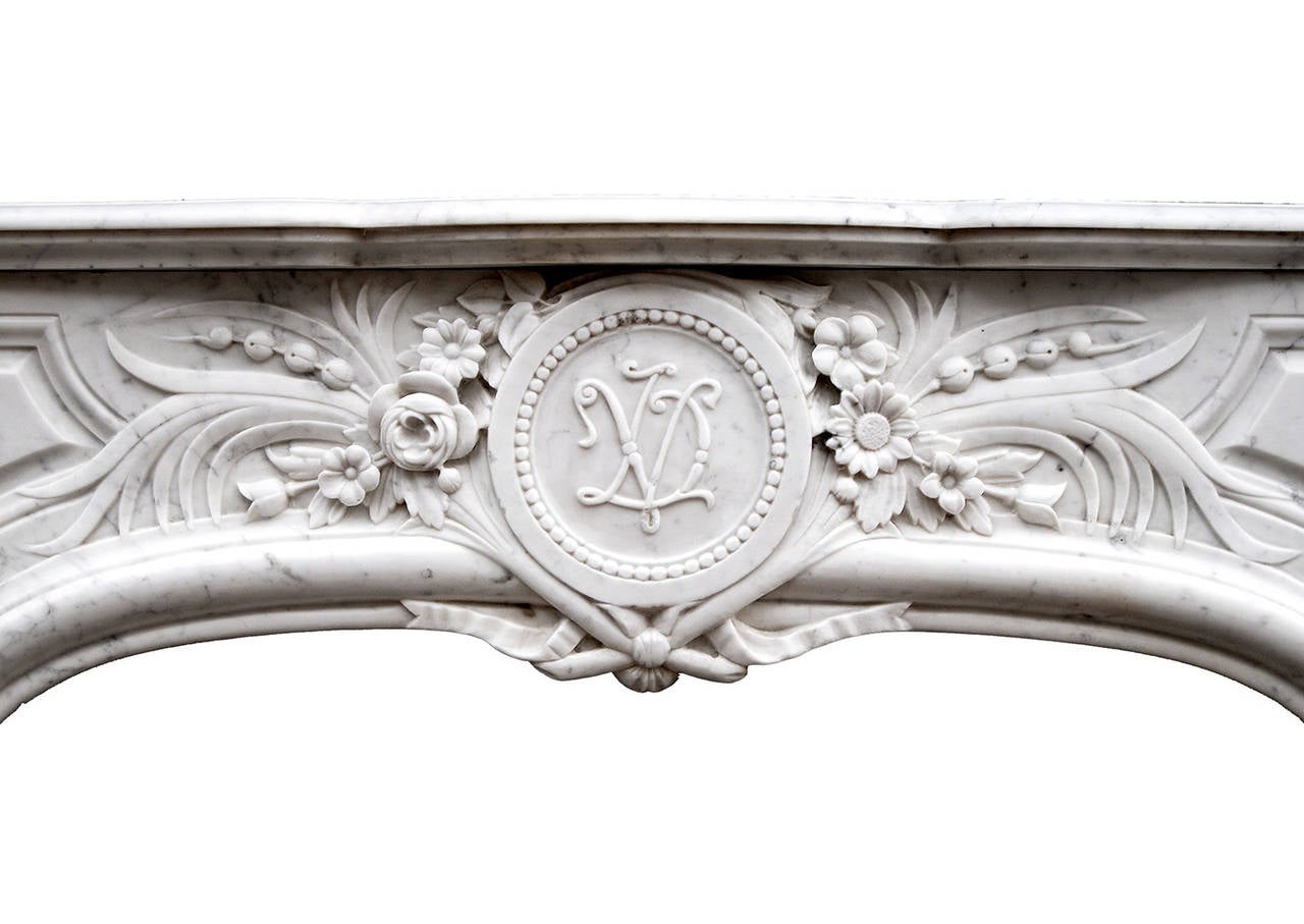 Une jolie cheminée en marbre de Carrare de style Louis XIV. La frise à panneaux est bien sculptée de fleurs et de feuillages, avec des rubans et un carquois sous une plaque circulaire centrale initiée. Les montants sont décorés de volutes et de