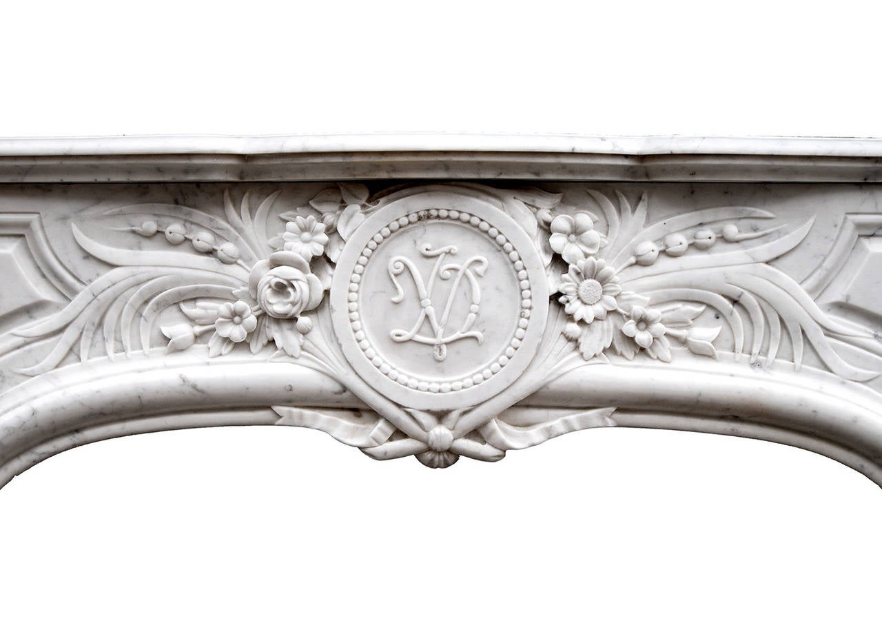 An attractive Louis XIV style Carrara marble fireplace. The panelled frieze with good carving of flowers and foliage, with ribbons and quiver below initialed centre circular plaque. The jambs with scrolls and leaf decoration, surmounted by carved