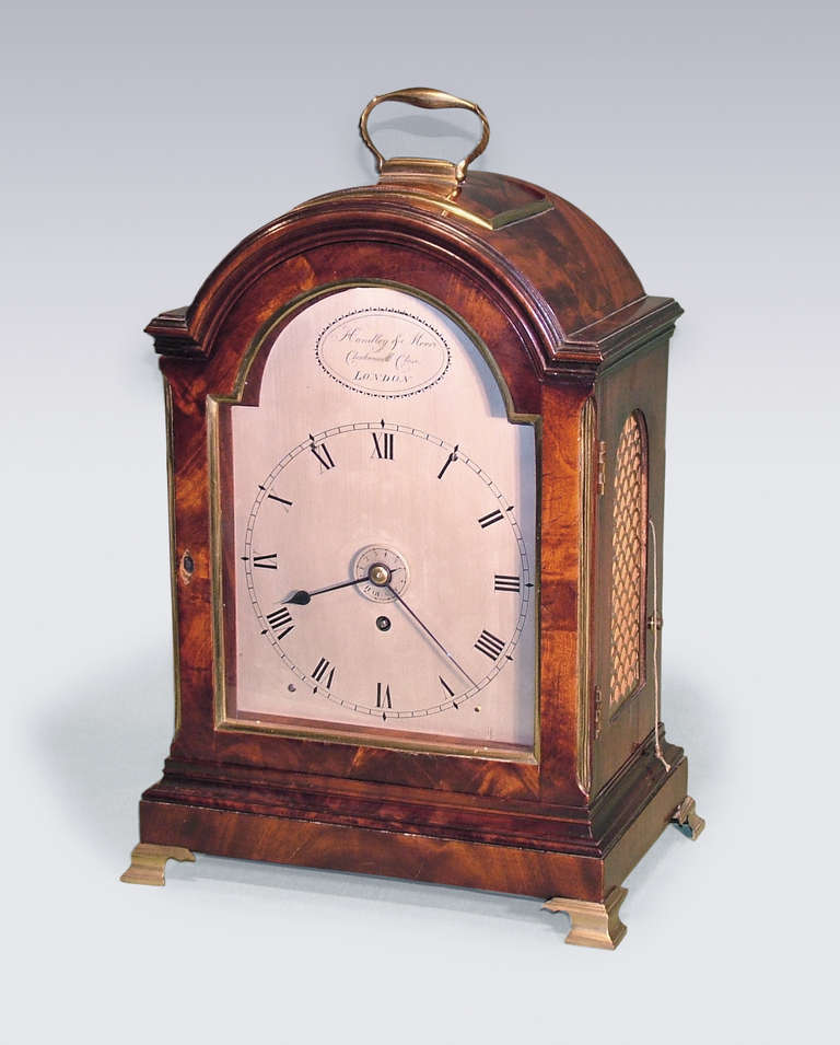 A fine quality early 19th century mahogany domed top bracket clock having brass carrying handle and moulded decoration raised on original brass ogee bracket feet retaining original mahogany wall bracket. The movement with silvered dial by “Handley