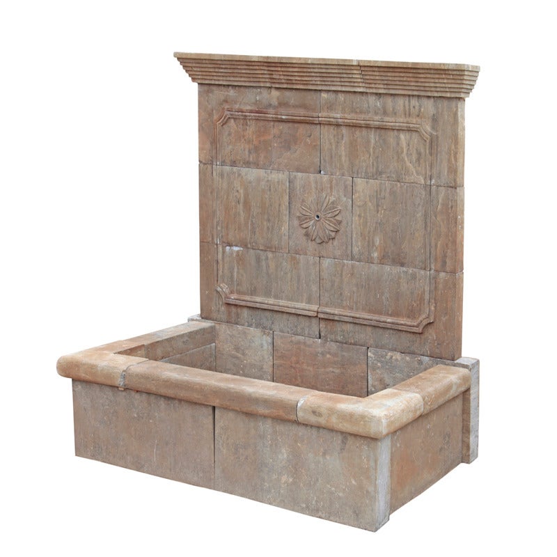 The fountain has a square basin and a wall piece with a stepped top part. Underneath is a coffered area with a flower ornament in its centre, out of which the water flows.
The basin has a slightly broader rim and a smooth wall. 

The fountain